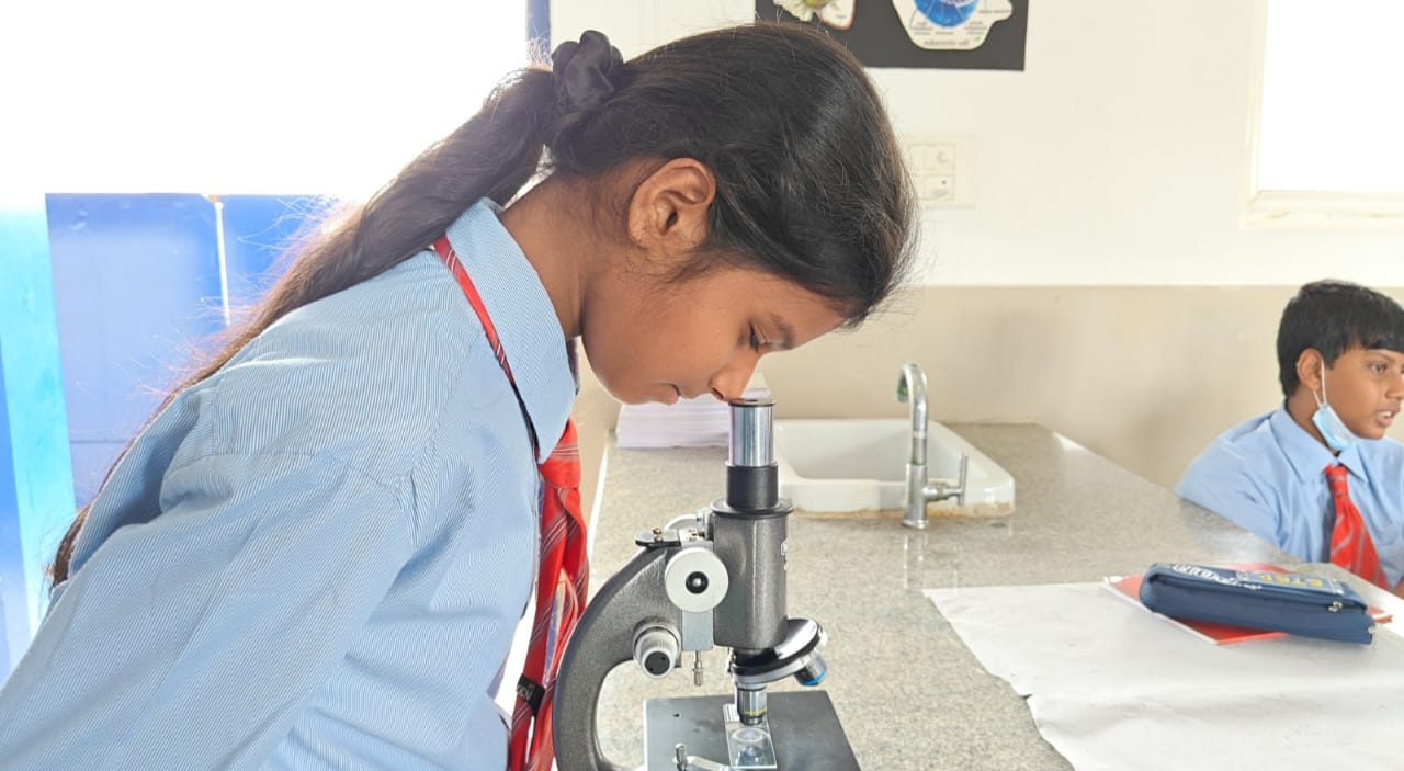 A student examining a specimen under a microscope in a science lab at Alpine School, a top CBSE school in South Bangalore.